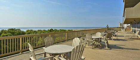 A wooden deck with tables and chairs, overlooking a beach.