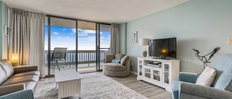 Ein Wohnzimmer mit Sofa, Sessel, Fernseher und Meerblick durch eine Schiebetür.