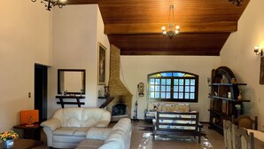 A spacious living room with a fireplace, a large window, and a wooden ceiling. - Come and relax in the second best climate in the world. (Atibaia)