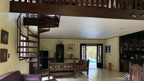 A spacious living area with a wooden staircase, a sofa, a coffee table, and a bookshelf. - Come and relax in the second best climate in the world. (Atibaia)