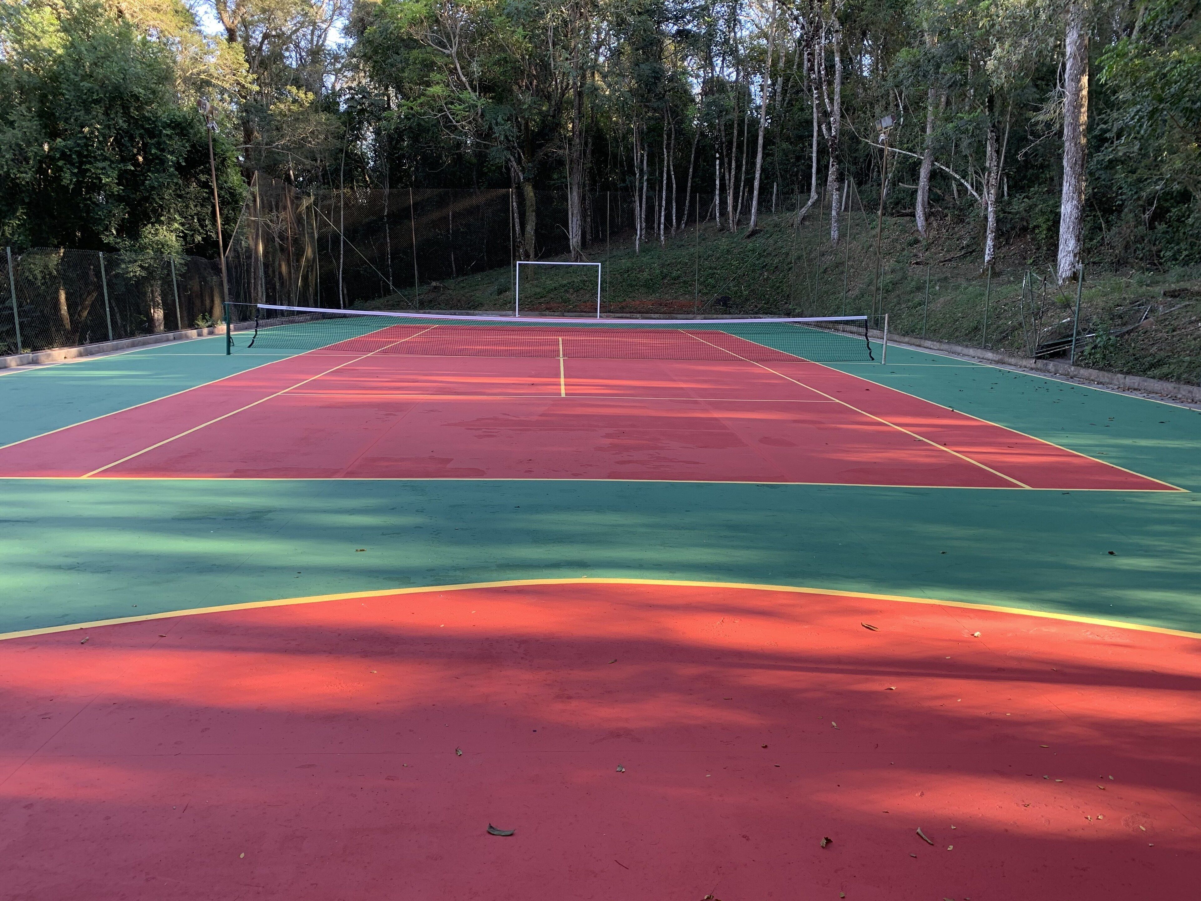 Een tennisbaan buiten met een net in het midden, omgeven door bomen.