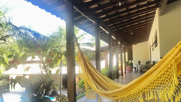 A covered outdoor area with a hammock, potted plants, and a tiled floor. - Come and relax in the second best climate in the world. (Atibaia)