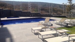 A swimming pool with lounge chairs and a stone wall. - Nuevo Lujoso Depto Residencial Queretaro (Querétaro)
