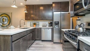 A modern kitchen with stainless steel appliances, dark cabinetry, and a central island. - At Base of Cottonwoods! * Private Hot Tub * Xbox (Cottonwood Heights)