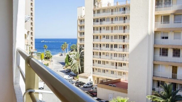 A high-rise building with multiple balconies, a view of the sea, and parked cars in the foreground. - MARE NOSTRUM - Apartment near the beach with private pool (Calp)