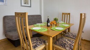 A dining area with a wooden table set for four, green placemats, and a bottle of wine. Chairs with patterned cushions surround the table. - MARE NOSTRUM - Apartment near the beach with private pool (Calp)