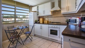 A modern kitchen with white cabinets, a gas stove, a microwave, and a dining area with a table and chairs. - MARE NOSTRUM - Apartment near the beach with private pool (Calp)