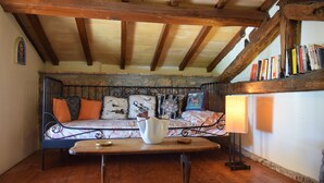 A cozy room with a wooden ceiling, a patterned sofa with cushions, a small table, and a wall-mounted bookshelf.