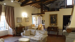 A spacious living room with a high ceiling, a dining area, and a staircase leading to an upper level.
