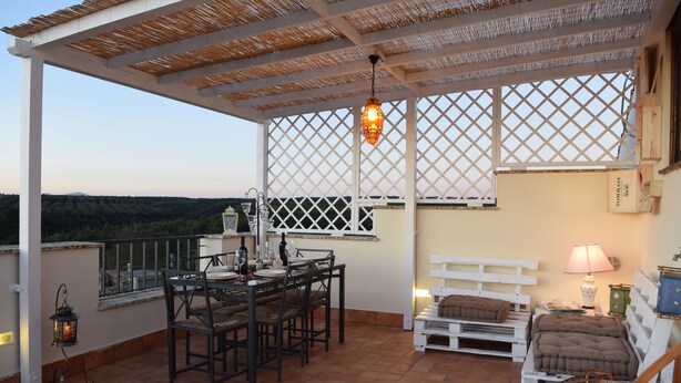 A covered patio with a table and chairs, a bed, and a lamp.