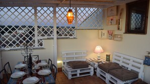 A cozy outdoor dining area with a table set for a meal, a white bench, and a hanging light fixture.