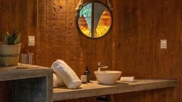 Un mur en bois, un miroir rond, un lavabo et un lit.