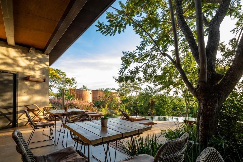 Un patio al aire libre con una mesa y sillas para comer, rodeado de vegetación y un árbol grande.