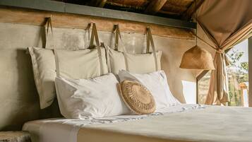 A bed with a wooden headboard, white bedding, and a woven basket hanging from the ceiling.