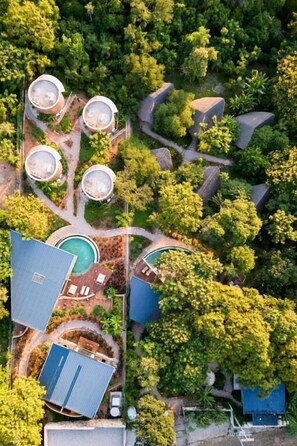 Vue aérienne d’une propriété comprenant plusieurs bâtiments, notamment un espace piscine et plusieurs structures circulaires qui pourraient être des réservoirs d’eau ou des locaux de stockage.