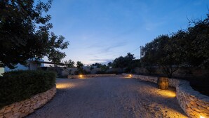 Un camino de grava flanqueado por muros de piedra y árboles, iluminado con luces en el suelo.