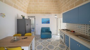 Una cocina compacta con armarios azules, un comedor con sillas amarillas y un sofá azul.