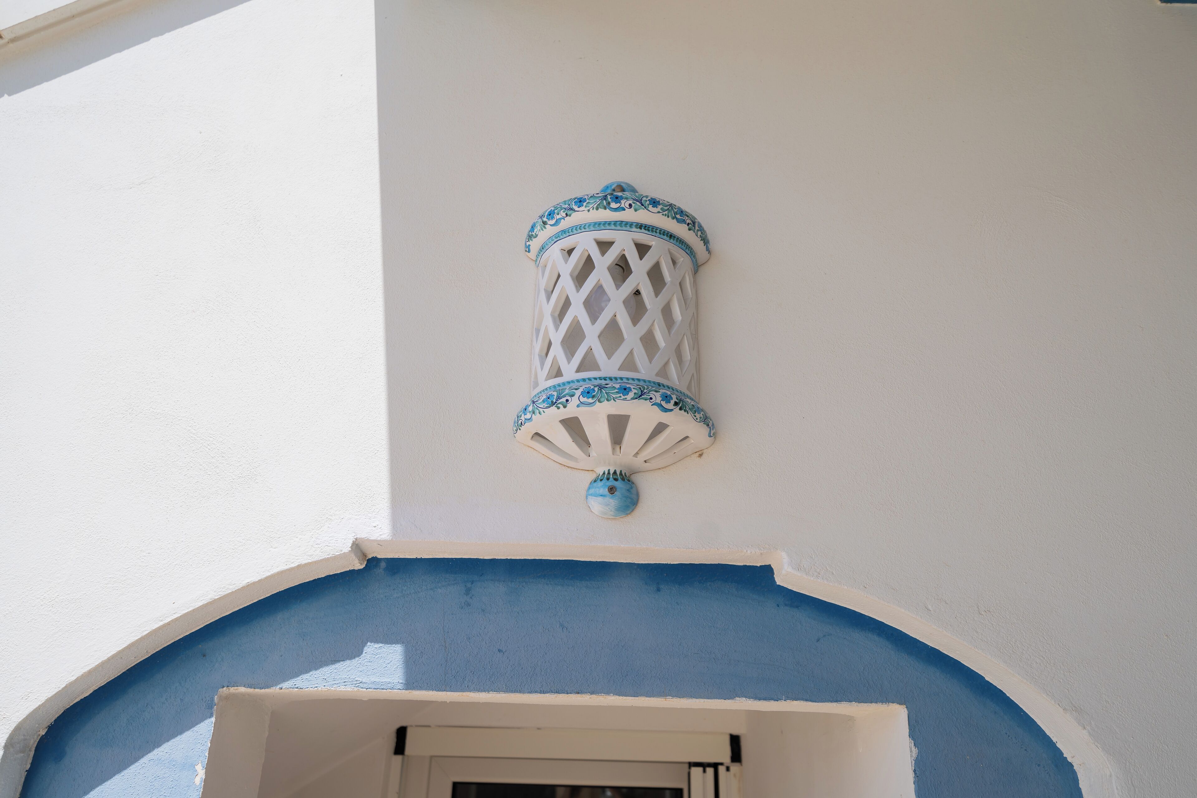 A white wall with a blue-painted archway and a decorative white lantern with blue accents.