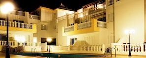 Ein mehrgeschossiges Hotel mit Balkonen, einem Swimmingpool und Außenbeleuchtung.