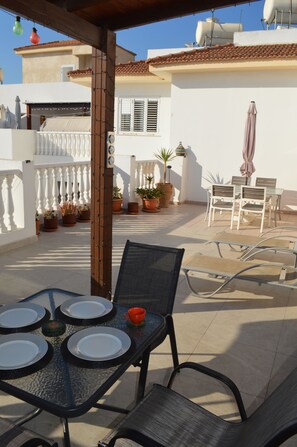 A patio with a table set for four, surrounded by chairs, and potted plants.