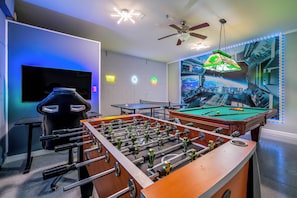 Una habitación con mesa de futbolín, mesa de billar, televisor y ventilador de techo.