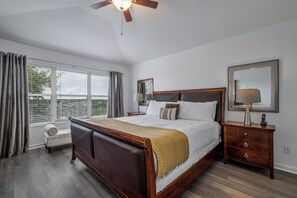 Un dormitorio con una cama grande, una mesita de noche, una lámpara, un espejo y una ventana con cortinas.