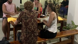 Un groupe de personnes est assis autour d’une table en bois dans une pièce dotée d’une fenêtre et d’une plante.