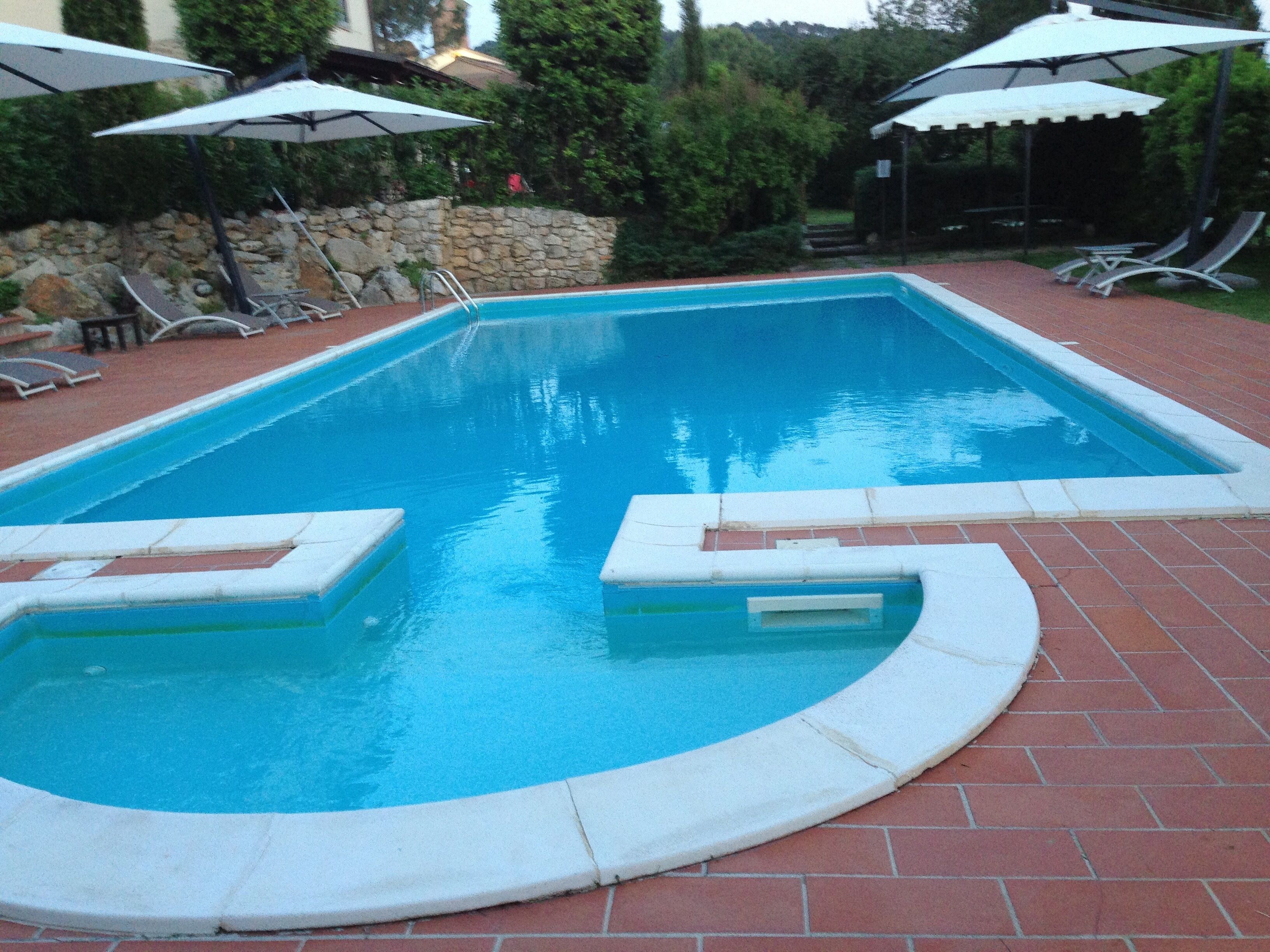 Une piscine rectangulaire bordée de briques, entourée de chaises longues et de parasols.