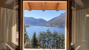 Una ventana de madera con vistas despejadas a un lago rodeado de montañas y árboles.