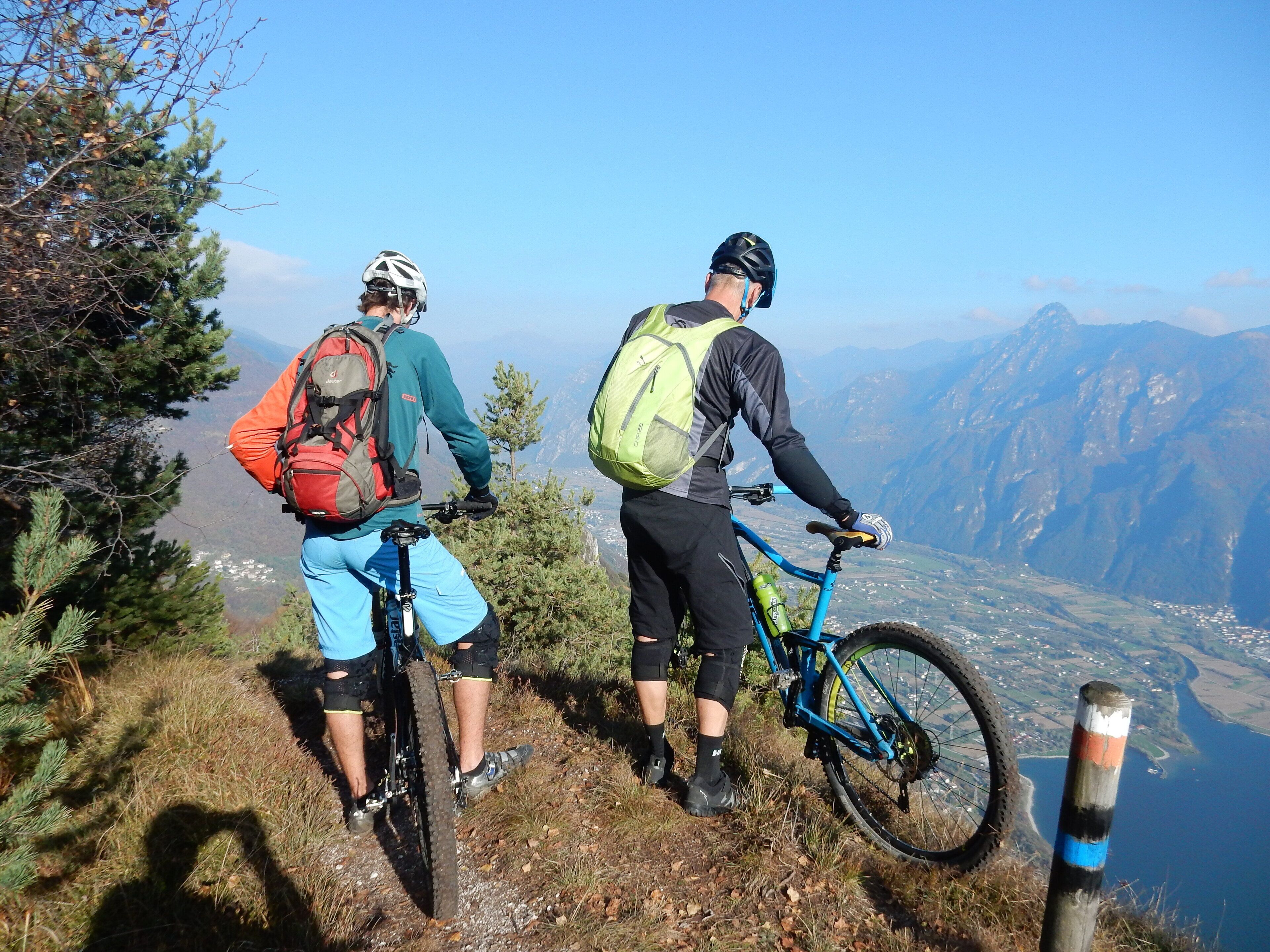Two people on a mountain trail with a view of a valley and mountains in the background.