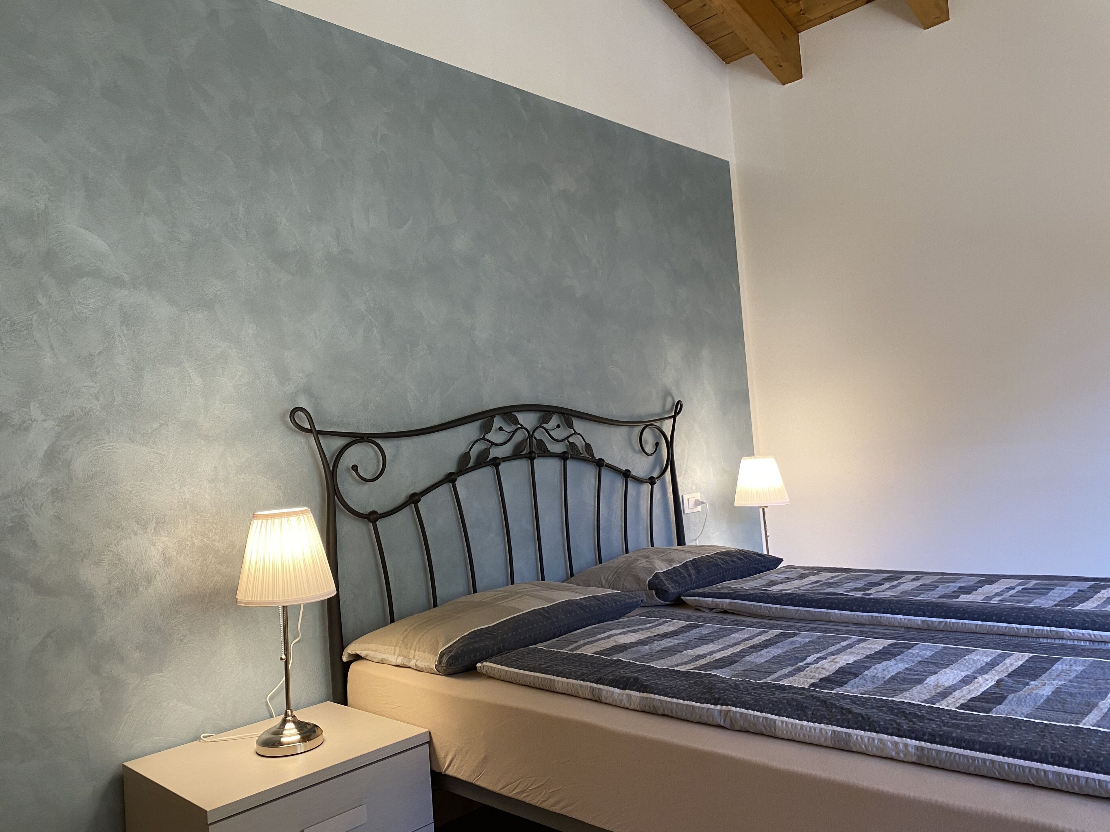 A bedroom with a bed, two bedside lamps, a nightstand, and a textured wall.