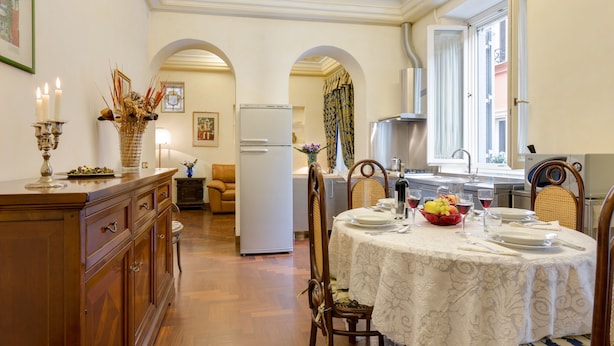 Un comedor con una mesa dispuesta para cuatro, un refrigerador y una cocina al fondo.