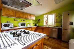 Une cuisine avec des meubles en bois, une cuisinière à gaz, un four à micro-ondes, un réfrigérateur et une fenêtre avec des rideaux.