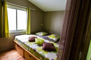 Un lit simple avec une couvre-lit à pois verts et blancs, deux oreillers et une table de chevet en bois avec des tiroirs.