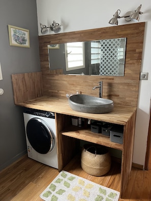 Une petite salle de bain avec un meuble-lavabo en bois, un lave-linge encastré, un grand miroir et un petit tapis.