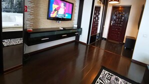 A modern living room with a flat-screen TV mounted on a wooden wall, a black entertainment unit, and a patterned rug on the floor. - Studio G by MRG Apartments | Steps away from Metro & Amenities (București)