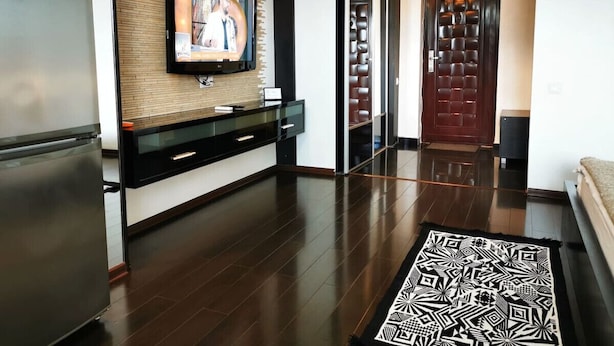 A modern kitchen with a built-in refrigerator, a wooden accent wall, and a flat-screen TV mounted above a black countertop. - Studio G by MRG Apartments | Steps away from Metro & Amenities (București)