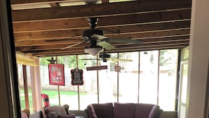 A covered outdoor seating area with a wooden deck, a red patterned rug, and a ceiling fan.