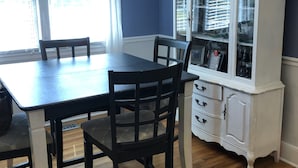 A dining area with a wooden table and chairs, a white cabinet with glass doors, and a window with blinds.