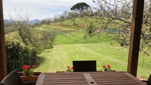 Un tavolo e sedie in legno sotto una pergola con vista su un campo verde e alberi.