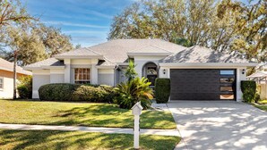 A single-story house with a dark garage door, a well-maintained lawn, and a mailbox. - Palm Harbor Paradise | Spacious Home with Pool & Hot Tub (Palm Harbor)