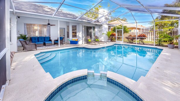 A swimming pool with a glass enclosure, surrounded by outdoor seating and potted plants. - Palm Harbor Paradise | Spacious Home with Pool & Hot Tub (Palm Harbor)