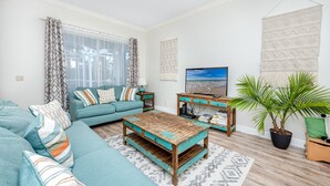 A living room with a teal sofa, a wooden coffee table, a TV, and a potted plant. - Palm Harbor Paradise | Spacious Home with Pool & Hot Tub (Palm Harbor)