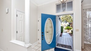 A hallway with a blue door, white walls, and a tiled floor. - Palm Harbor Paradise | Spacious Home with Pool & Hot Tub (Palm Harbor)