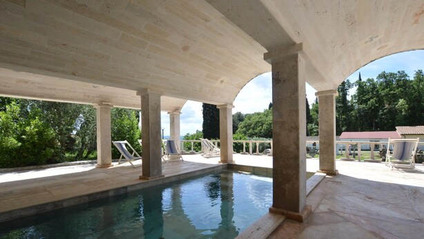 Une piscine intérieure à l’eau claire, entourée de colonnes de pierre et dotée d’un espace abrité avec des chaises longues.