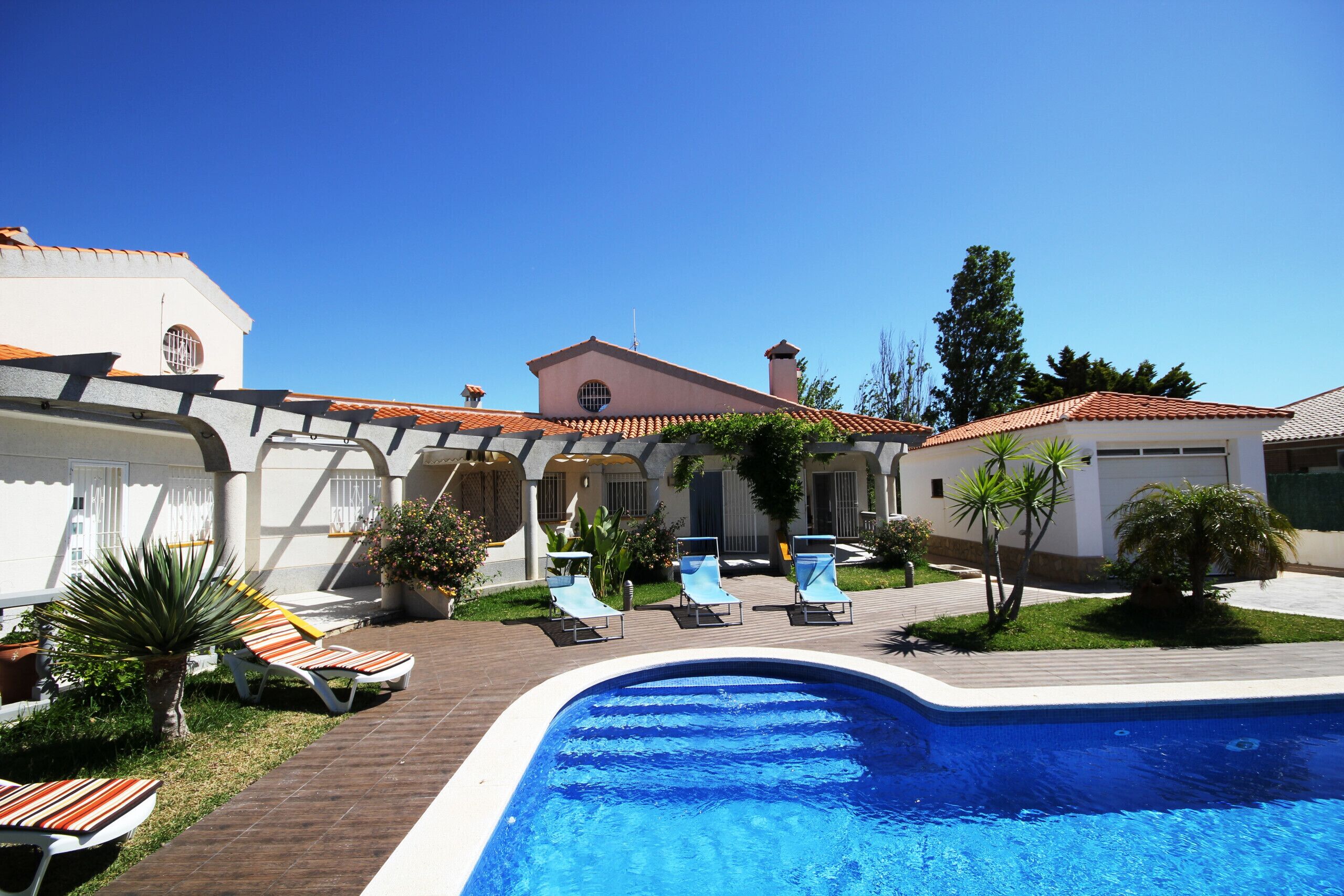 A swimming pool with lounge chairs, a brick pathway, and a building with a tiled roof.