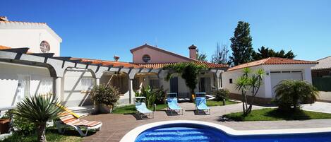 A swimming pool with lounge chairs, a brick pathway, and a building with a tiled roof.