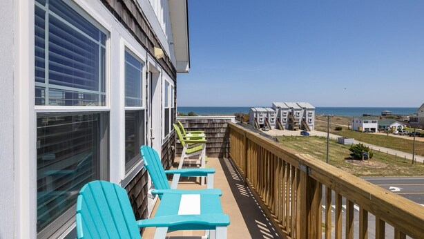 Ein Balkon mit blauen Stühlen und einem Tisch mit Blick auf einen Strand und den Ozean.