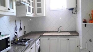 Una cocina con armarios blancos, estufa a gas, microondas y pileta.