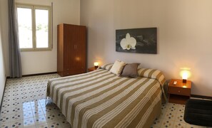 Ein Schlafzimmer mit einem Bett, zwei Nachttischen mit Lampen, einem Kleiderschrank, einem fußbodenbdecker mit Blumenmuster und einem an der Wand hängenden Blumenbild.